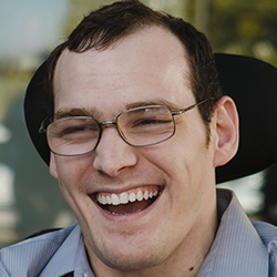 Image of Tomas Davis. Tomas is wearing wire rim glasses and is joyfully smiling.